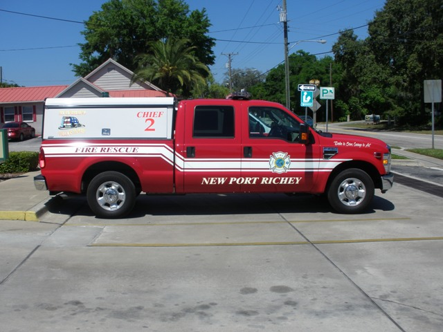 A red pickup truck with a tool topper on the bed. Text on the side reads: "Chief 2. Fire Rescue. New Port Richey."