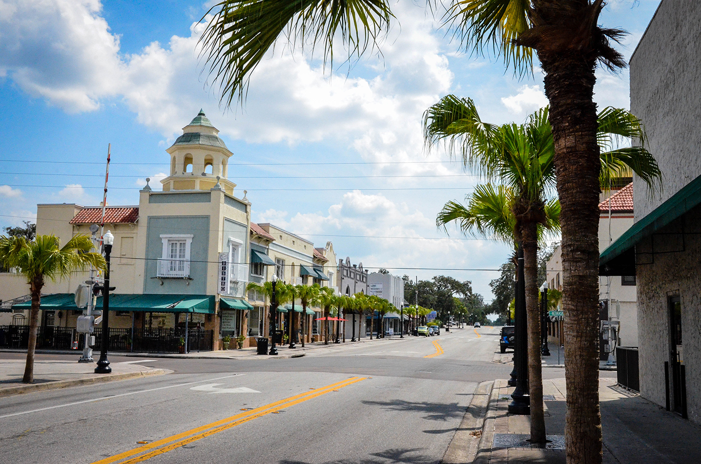 Street corner on a sunny day featuring a building with a cupola atop it. Palm trees dominate the foreground.