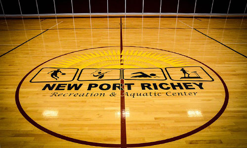Indoor Baseketball court at the half court with the City of new port richey recreation center seal in the middle.