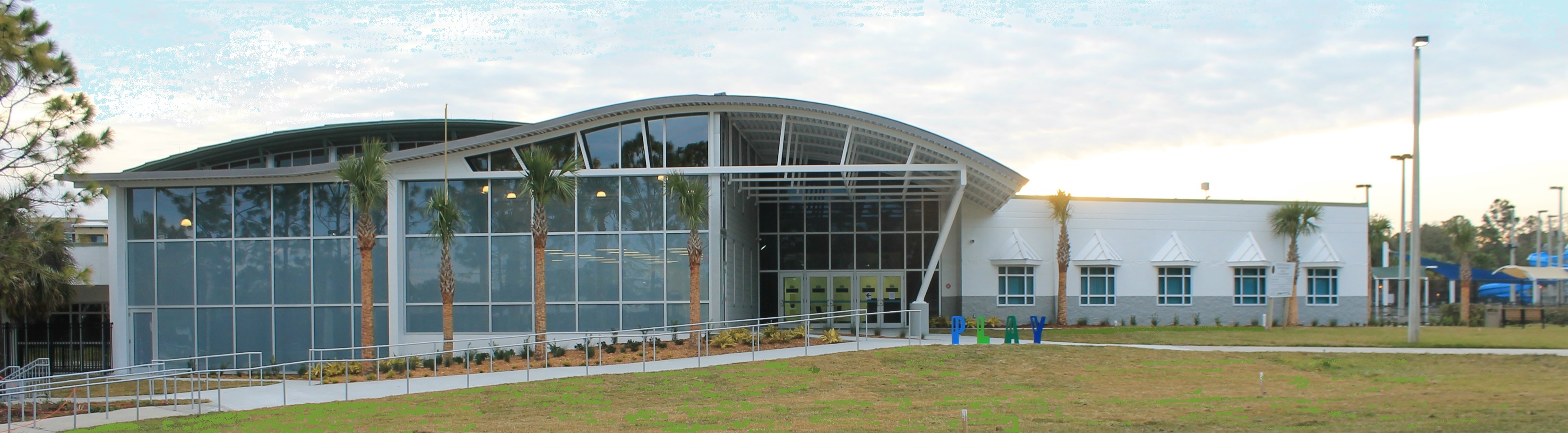 Front view of the Recreation and Aquatic Center. Floor to ceiling windows and a curved roof/awning are prominent.