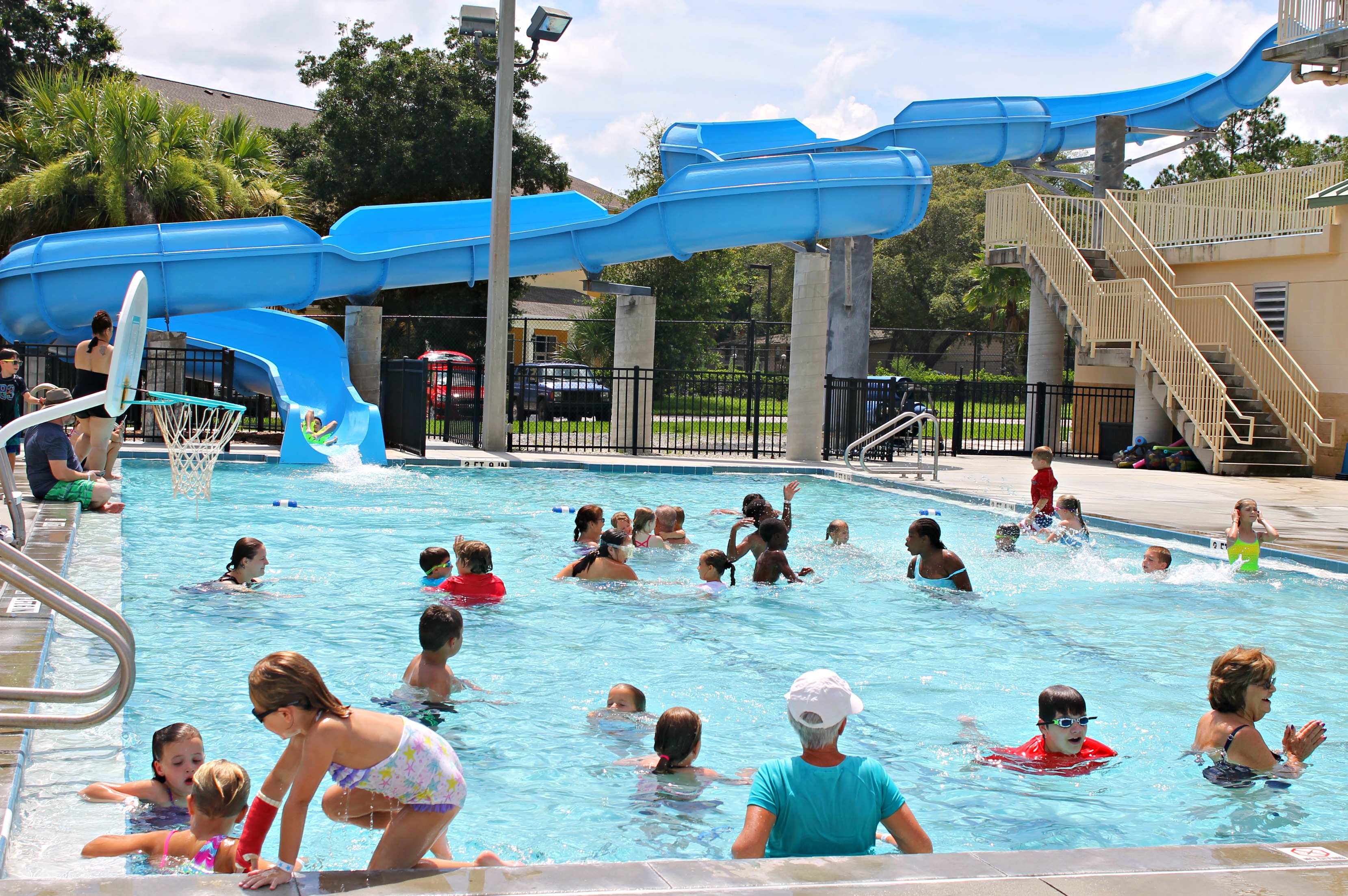 Swimming pool with a large waterslide leading into it. There are several active people in the pool.