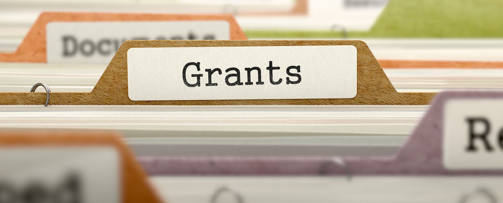Closeup of hanging file tabs. A tab with the word "Grants" typed on a label is the main focus.
